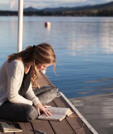 brygga i en sjö en flicka sitter och läser en bok på bryggan