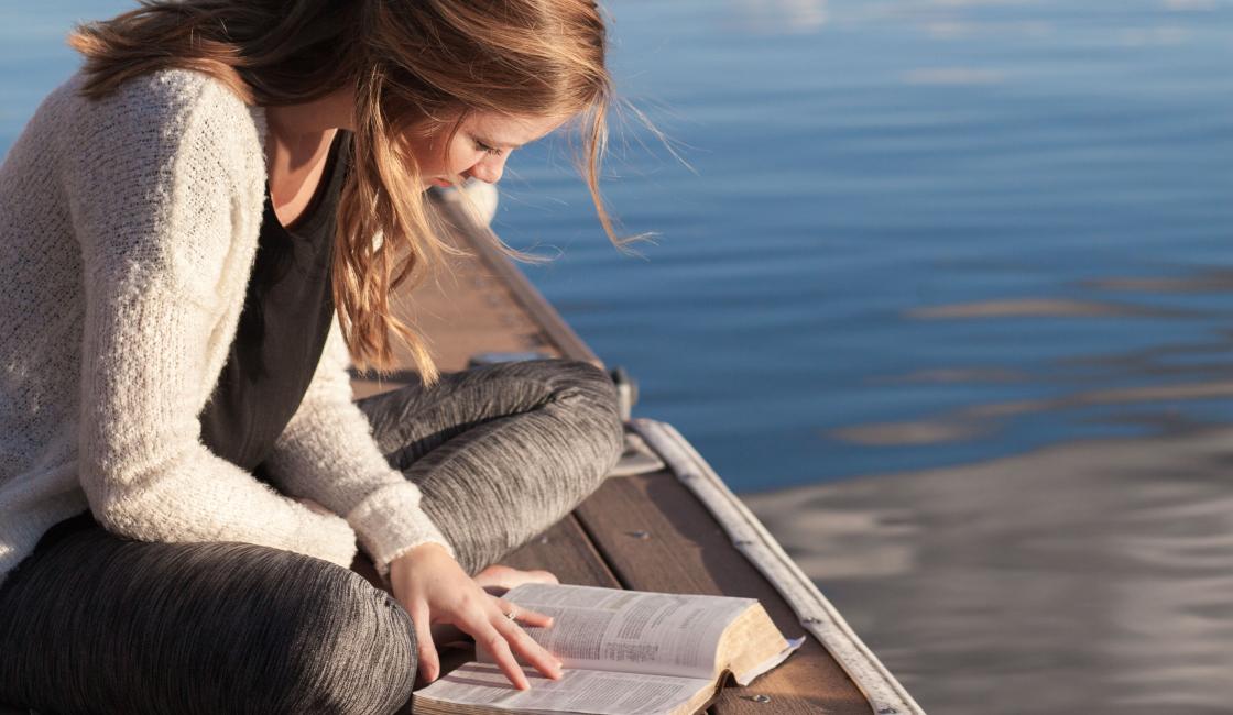 brygga i en sjö en flicka sitter och läser en bok på bryggan